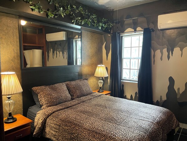 A bedroom with a bed, two bedside lamps, a mirror, a window with curtains, and a wall with a dripping paint design.