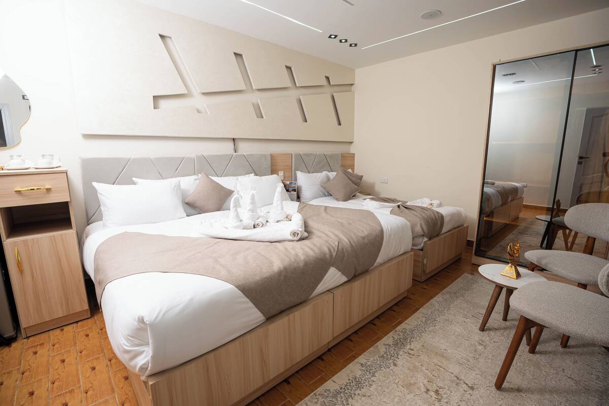 Una habitación de hotel moderna con una cama grande, una mesita de noche, un espejo y una zona de estar con sillas.