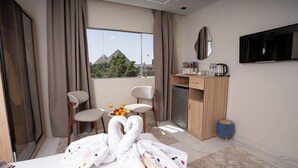Ein Hotelzimmer mit einem Bett, zwei Stühlen, einem Schreibtisch mit Kaffeemaschine, einem Fernseher und Blick auf die Pyramiden.