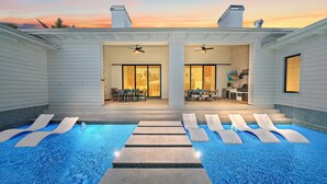 A swimming pool with lounge chairs, a patio area with a table and chairs, and a kitchen area with a TV and grill. - Luxury Resort-Like Home at St. Armands Circle and Lido Key Beach (Sarasota)