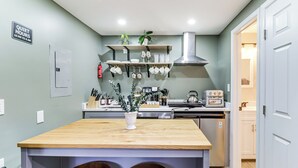 Une cuisine avec un îlot central en bois, deux tabourets, un porte-ustensiles suspendu et un panneau indiquant les heures de silence.