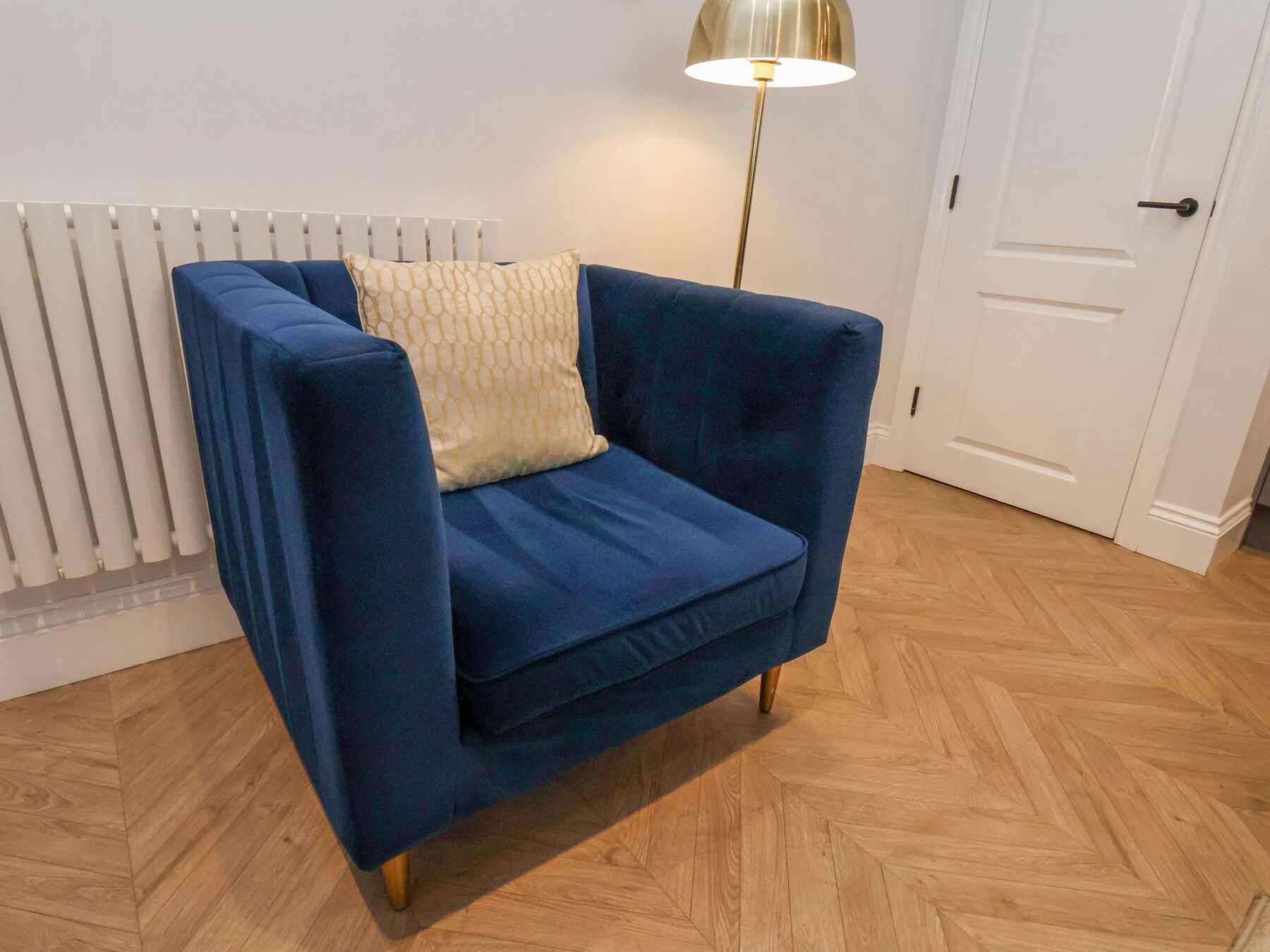 A blue armchair with a patterned cushion, positioned in front of a radiator and a door.