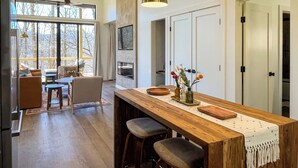 Eine moderne Küche mit einer Holztheke, Barhocker, Pendelleuchten und Blick ins Freie.