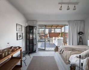 A modern bedroom with a large bed, a wooden side table, a glass door leading to a balcony, and a city view. - Historic Beauty Blends with Modern Design (Tel Aviv-Yafo)