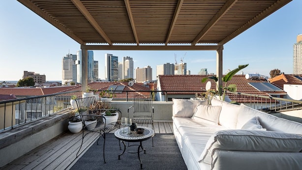 Een terras op het dak met een houten pergola, een witte bank, een ronde tafel en potplanten.