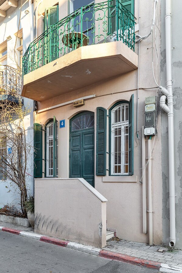 A building with a balcony, a door, and a window with shutters.