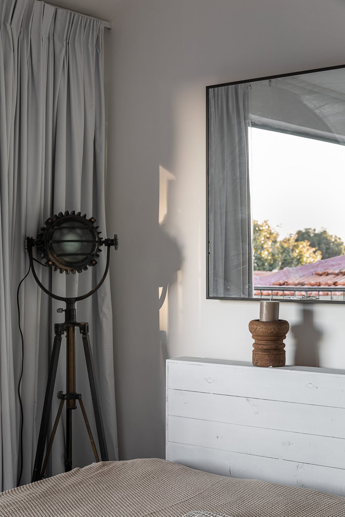 Ein Zimmer mit einem Bett, einem Fenster mit Blick auf Gebäude, einem Stativ mit einer Kamera und einem hölzernen Gegenstand auf dem Heizkörper.