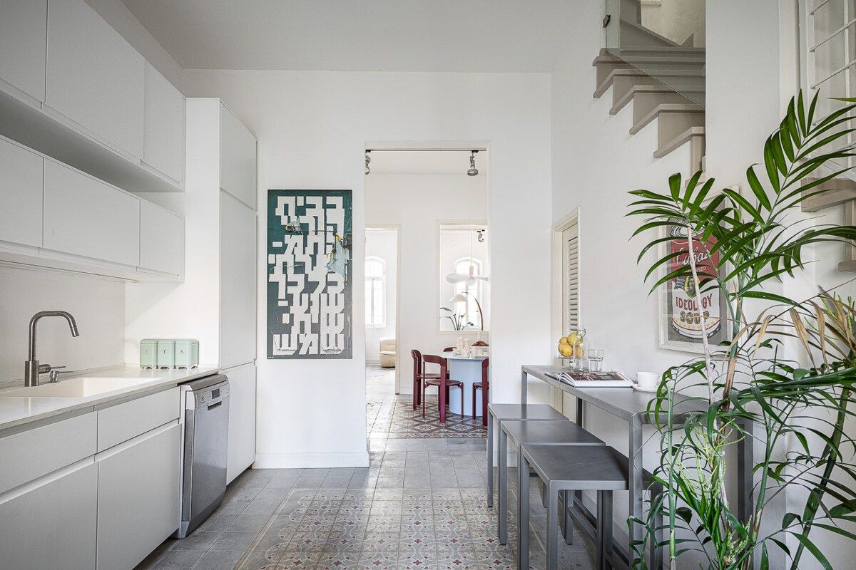 Una cocina moderna con armarios blancos, lavavajillas y un comedor con mesa y sillas.