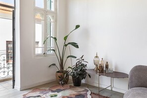 A room with a large window, a potted plant, a small round table with a lamp, and a chair.