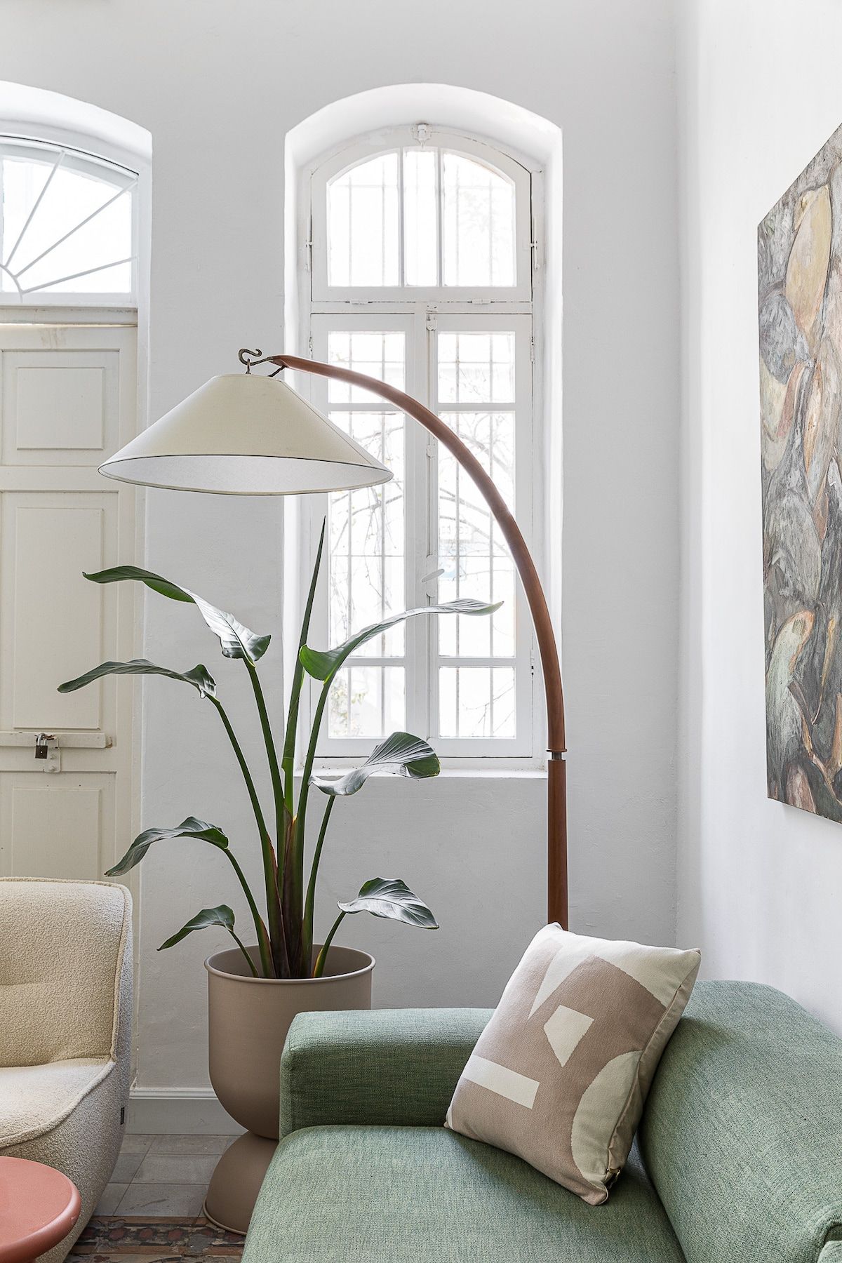 Ein Zimmer mit einem grünen Sofa, einem Blumentopf, einer Stehlampe und einem Fenster mit Blick.