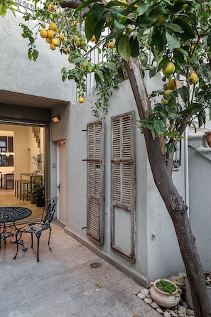 A courtyard with a table and chairs, a tree with lemons, and a building with shutters. - Historic Beauty Blends with Modern Design (Tel Aviv-Yafo)
