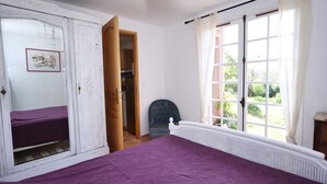 A bedroom with a bed, a wardrobe, a chair, and a window with a view of greenery.