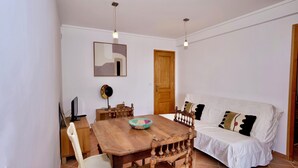 A dining area with a wooden table and chairs, a white sofa with patterned cushions, and a wooden door.