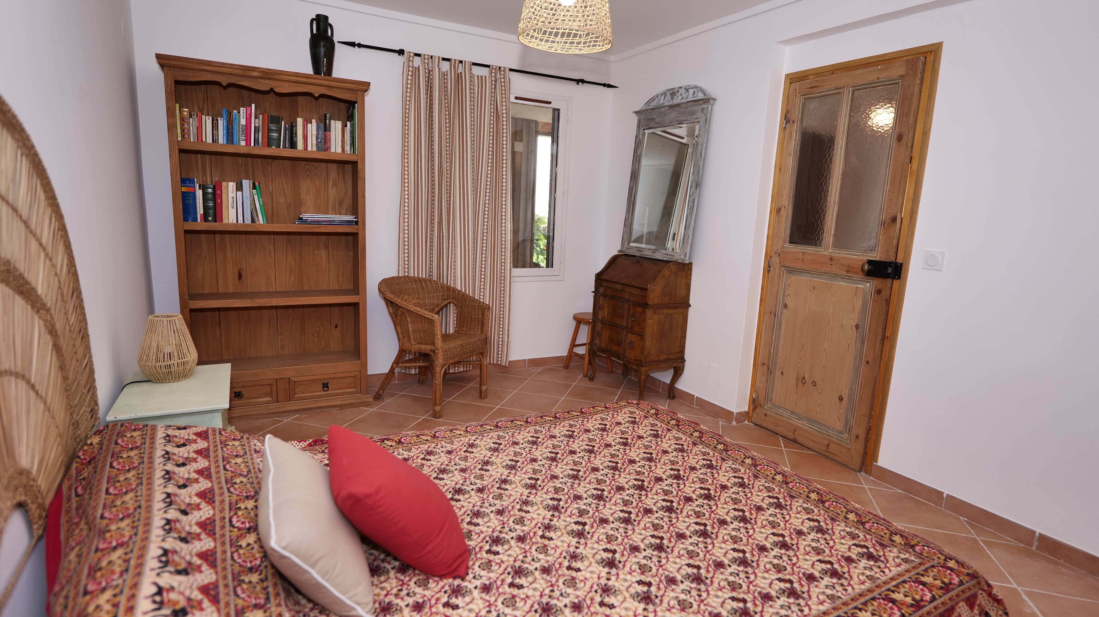 A room with a bed, a bookshelf, a chair, a dresser, a mirror, and a door.