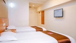Habitación de hotel con dos camas, cada una con cabecero marrón y ropa de cama blanca. Se aprecia un cuadro enmarcado en la pared y una puerta al fondo.