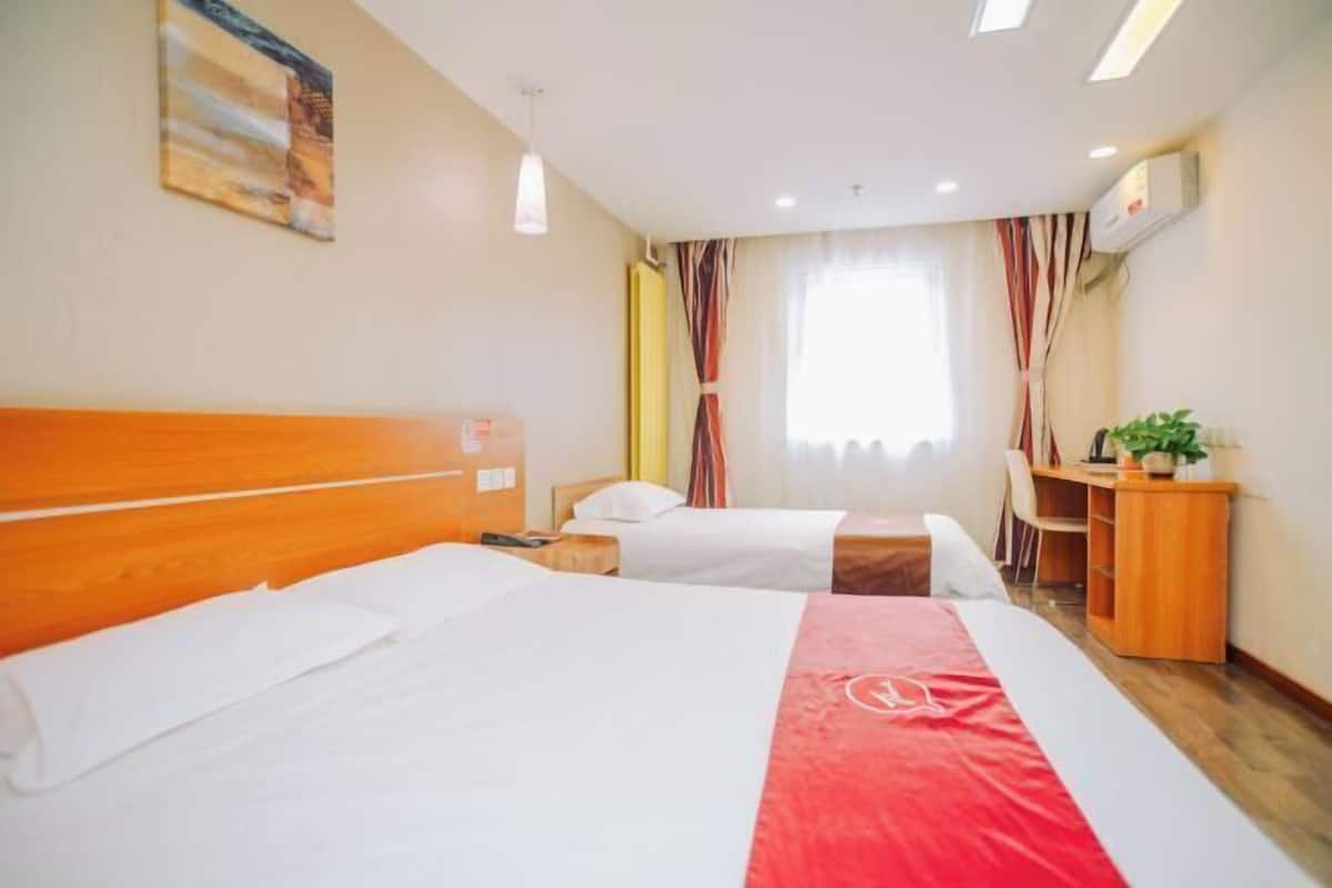 A hotel room with two beds, a desk, a chair, and a plant.