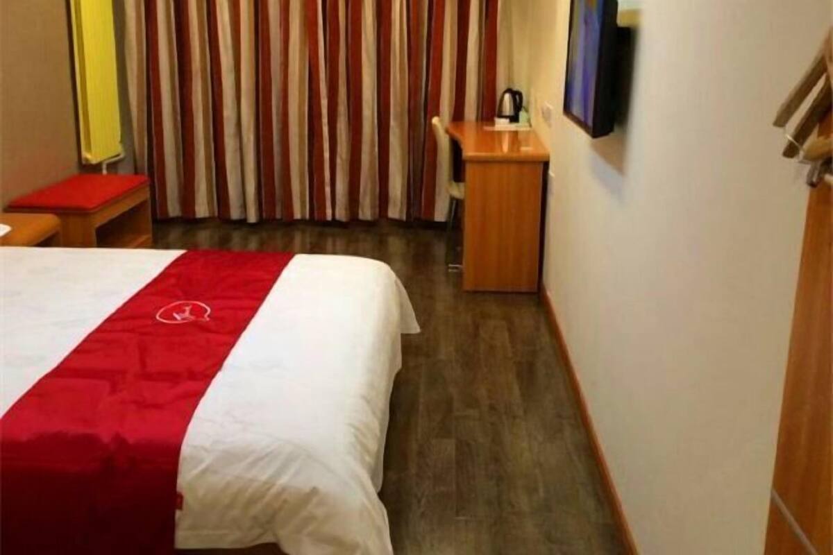A hotel room with a bed, a desk, a chair, a television, and a curtain.