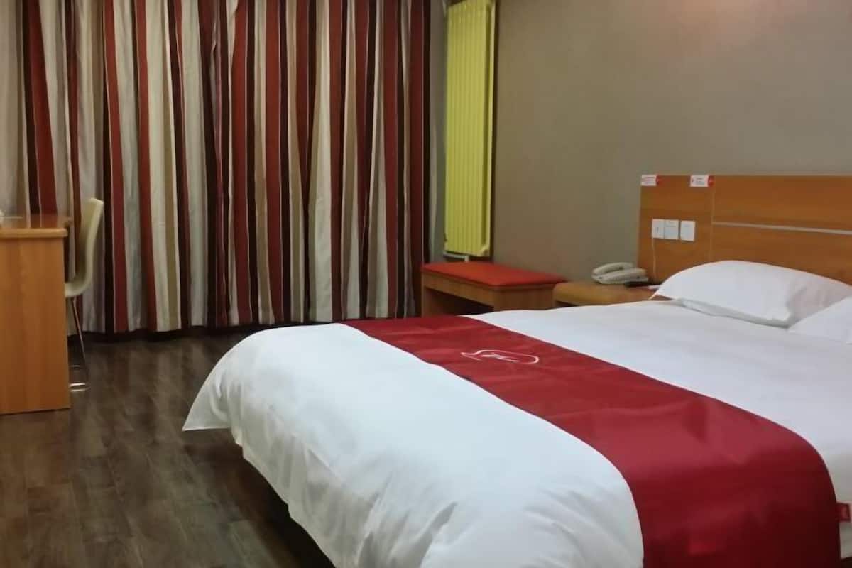 A hotel room with a bed, a desk, a chair, a telephone, and curtains.