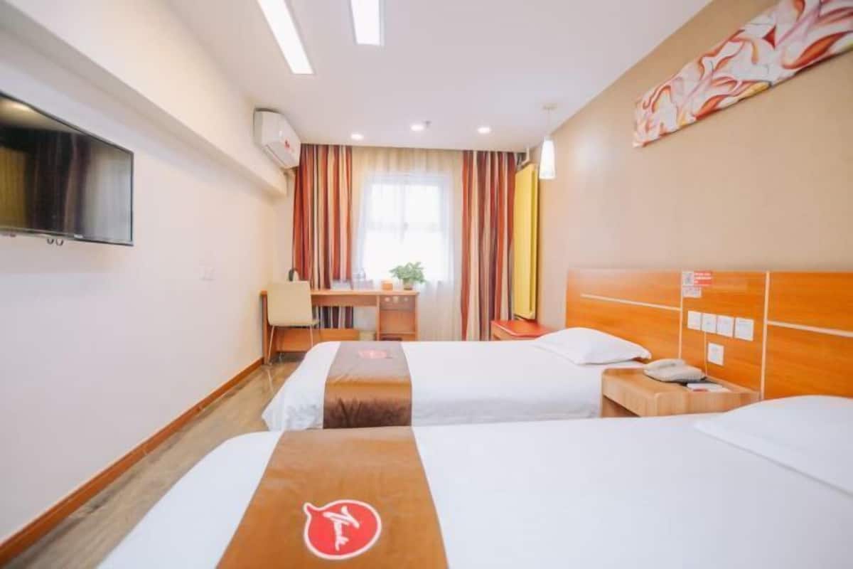 A hotel room with two beds, a desk, a chair, a TV, and a window with curtains.