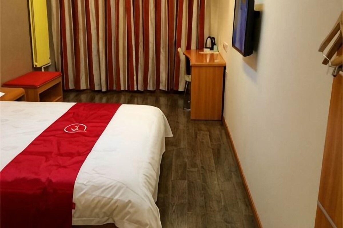 A hotel room with a bed, a desk, a chair, and a television.