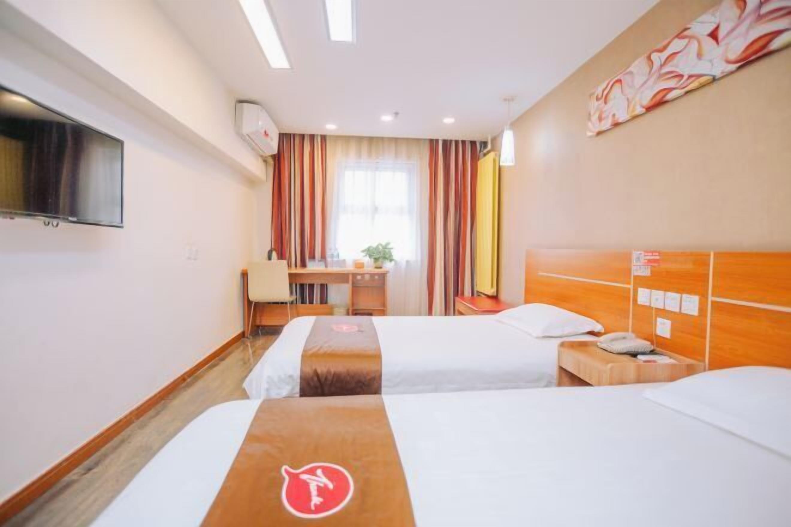 Quarto de hotel com duas camas, uma escrivaninha, uma cadeira, uma TV e uma janela com cortinas.