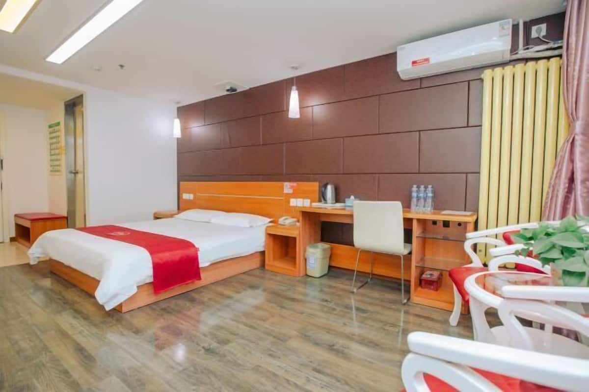A hotel room with a wooden bed, a desk with a chair, a small table, and a radiator.