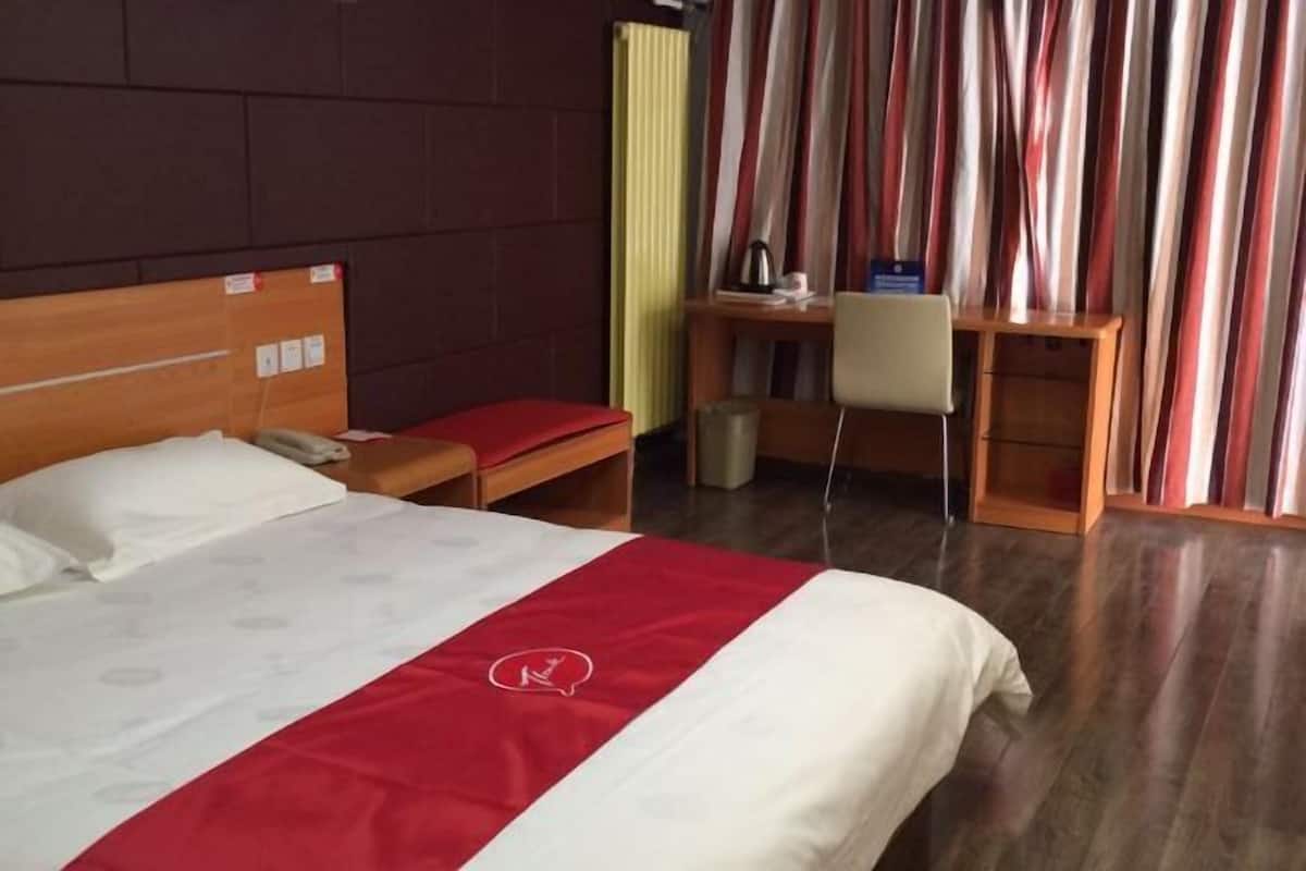 A hotel room with a bed, a desk, a chair, and a radiator.