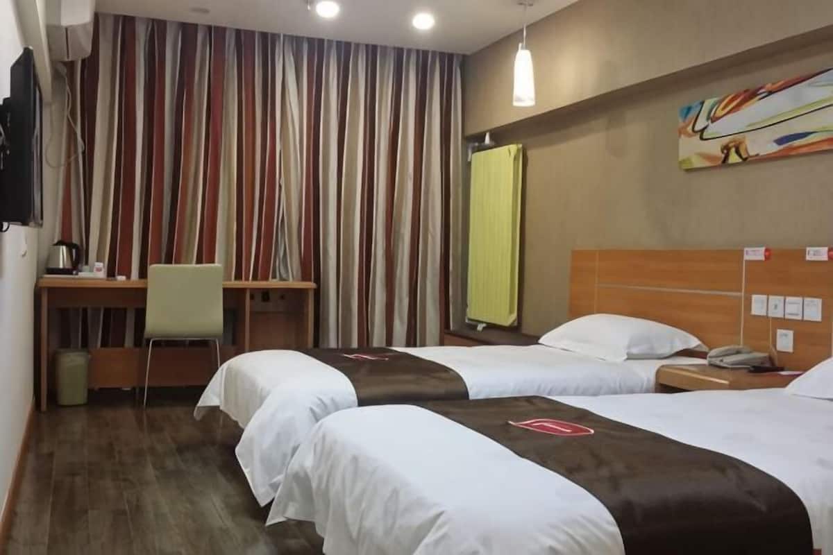 A hotel room with two beds, a desk, a chair, a TV, and a painting on the wall.