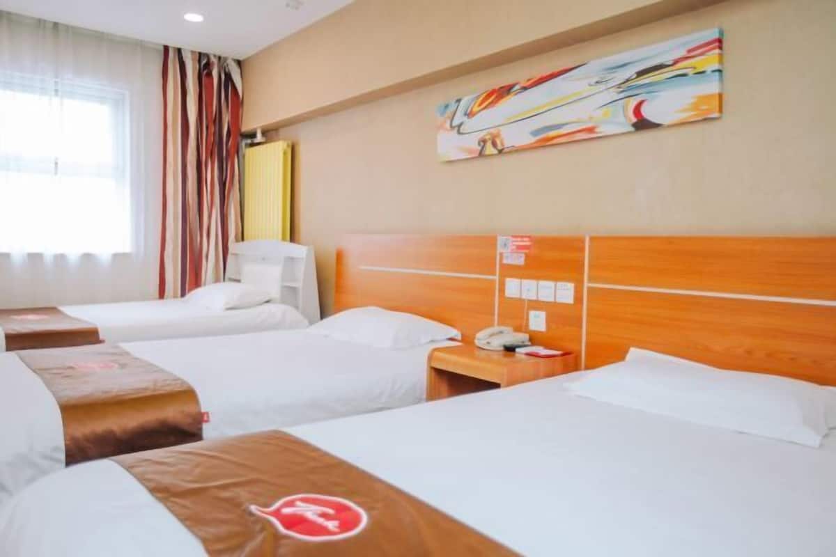 A hotel room with three beds, a wooden headboard, a bedside table with a phone, and a painting on the wall.