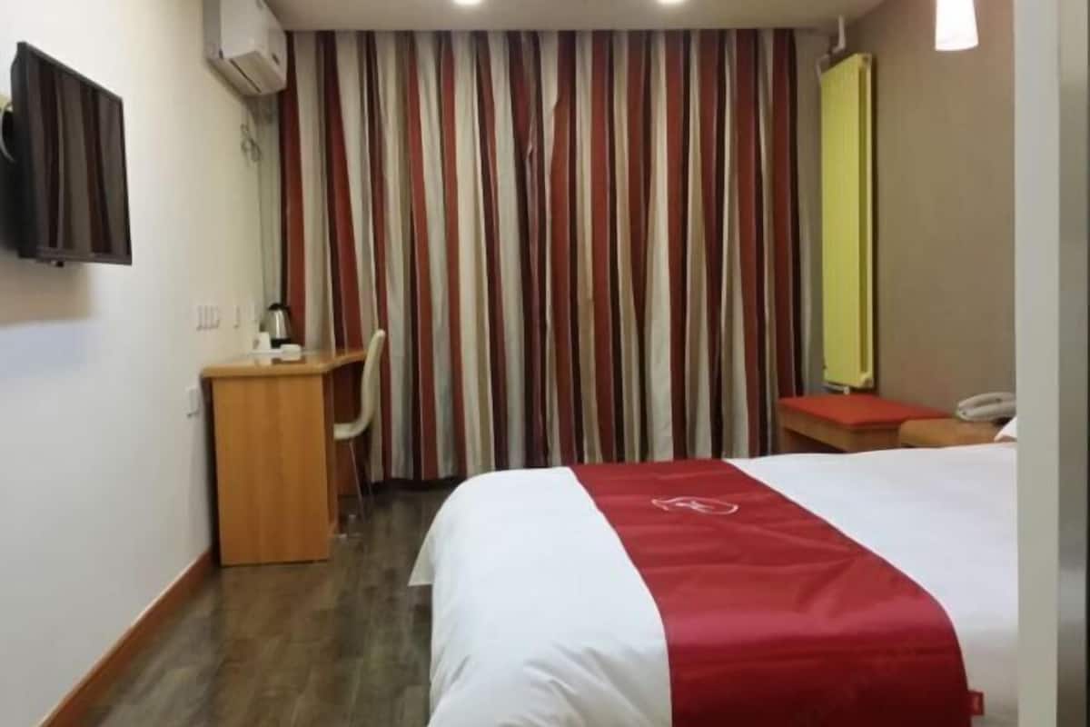 A hotel room with a bed, a desk, a chair, a telephone, and a striped curtain.