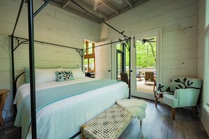 Ein Schlafzimmer mit einem Himmelbett, einer Bank und einem Sessel. Eine Tür führt zu einem Außenbereich mit Tisch und Stühlen.
