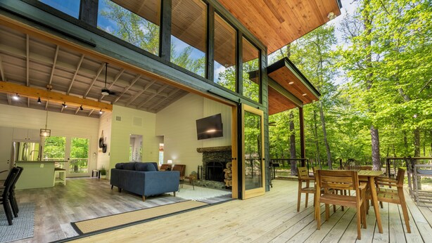 A spacious living area with a fireplace, wooden furniture, and large windows overlooking a forest.