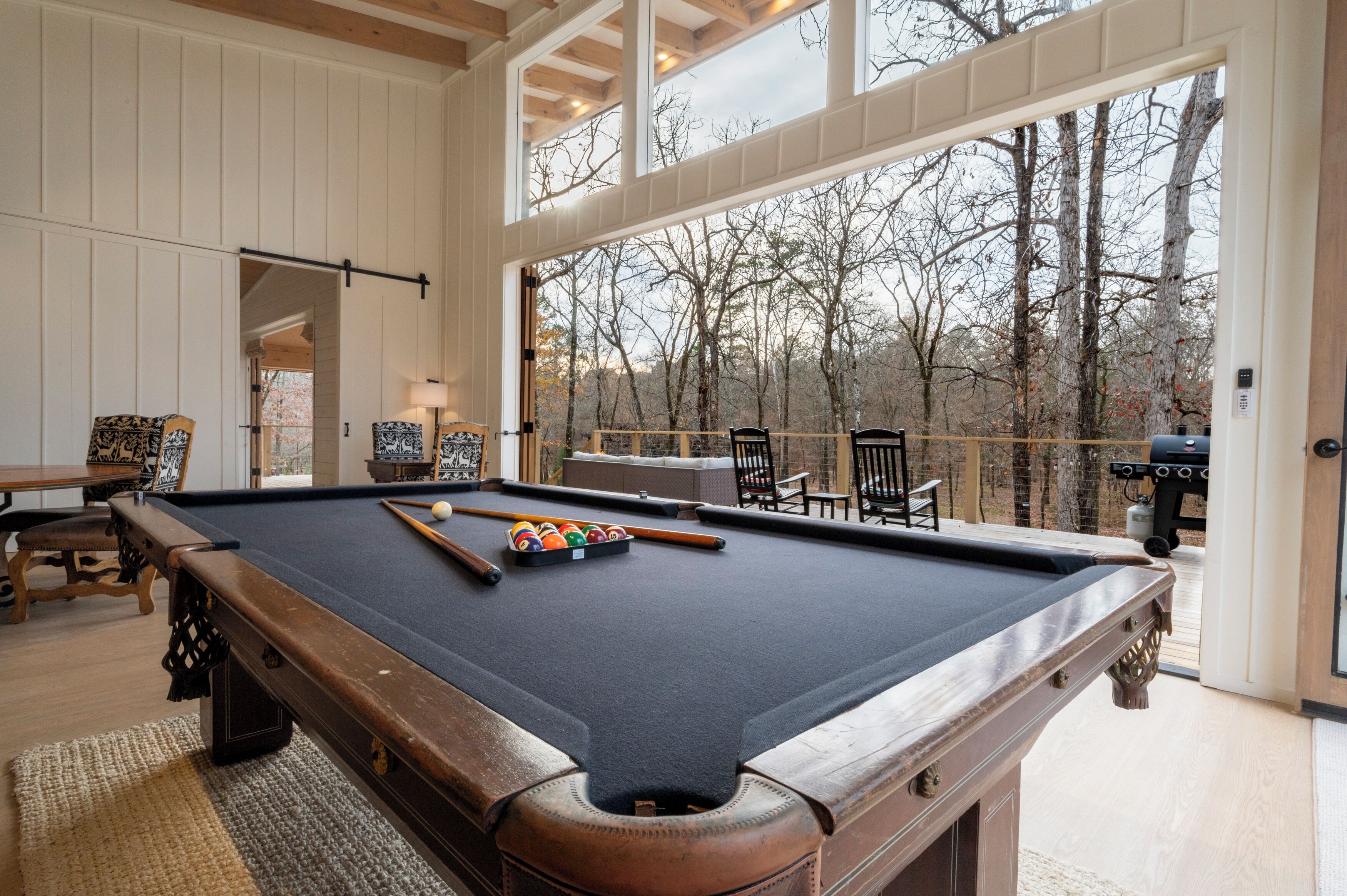 A pool table in a room with large windows overlooking a forest.