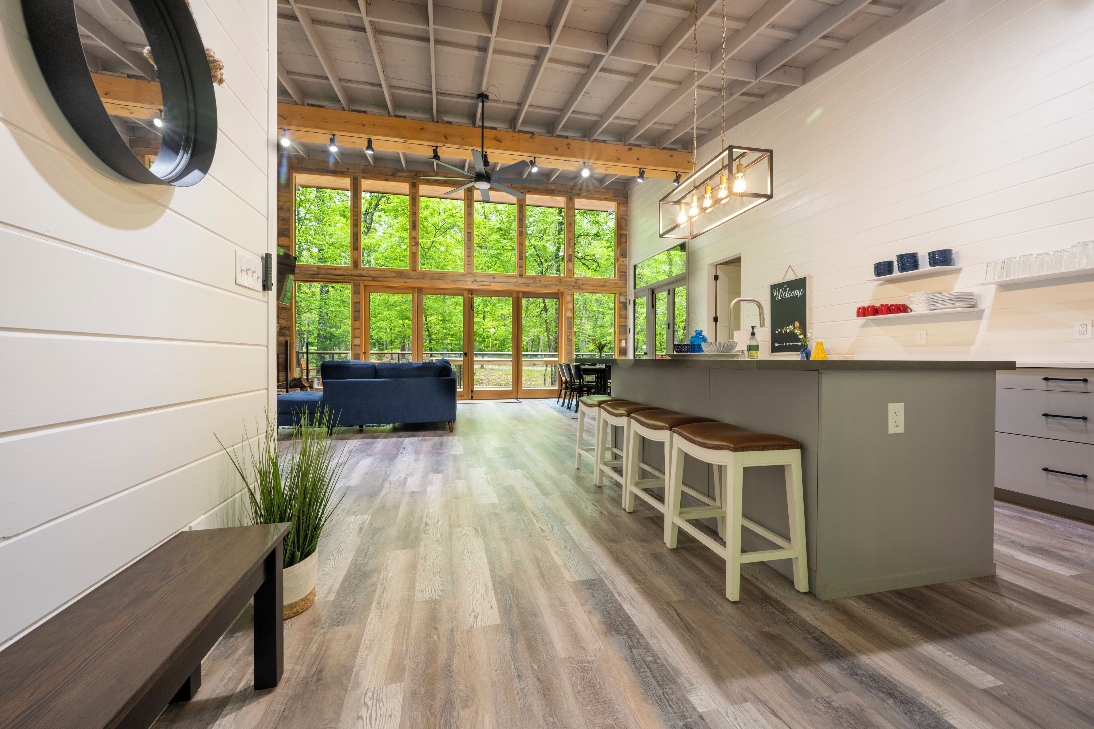 A modern kitchen with a central island, bar stools, and a view of the outdoors through large windows.