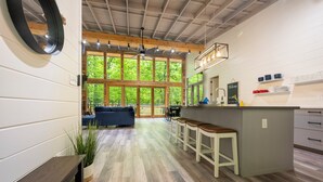 A modern kitchen with a central island, bar stools, and a view of the outdoors through large windows.