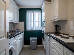 Enjoy cooking in this kitchen with oven and stovetop, featuring classic cabinetry and a convenient window with vertical blinds.