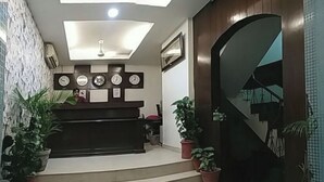 A reception area with a desk, multiple clocks, and potted plants. - The Hotel Vagmi (Gurugram)