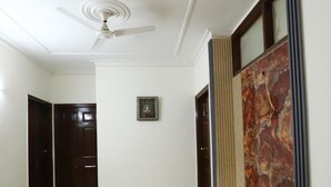 A hallway with a ceiling fan, a framed picture on the wall, and a marble-patterned wall panel. - The Hotel Vagmi (Gurugram)
