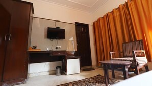 A hotel room with a wooden wardrobe, a small desk with a television, a chair, and a patterned rug. - The Hotel Vagmi (Gurugram)