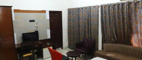 Una camera d'albergo con un letto, una scrivania, una sedia, un divano, una ventola a soffitto e tende.