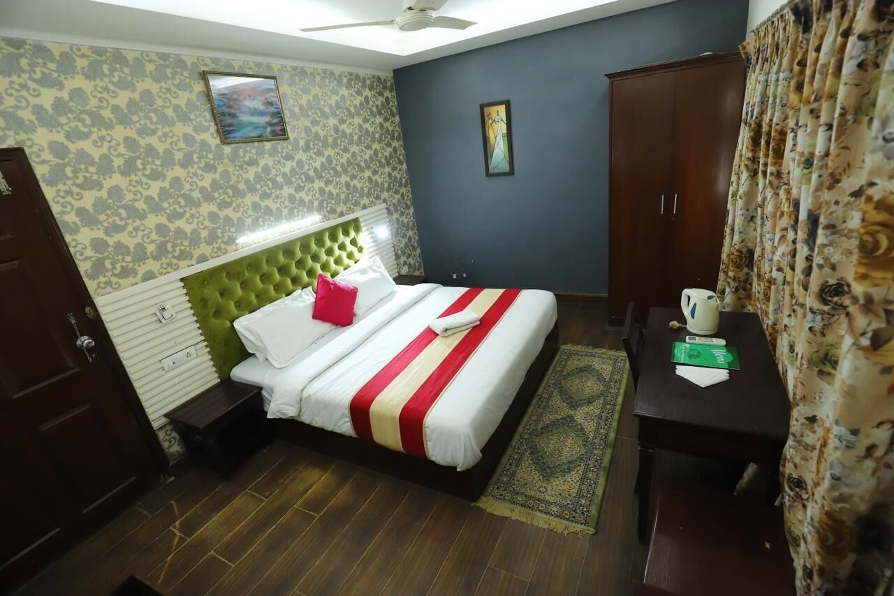 A bedroom with a bed, a green headboard, a nightstand, a wardrobe, and a small table with a kettle.
