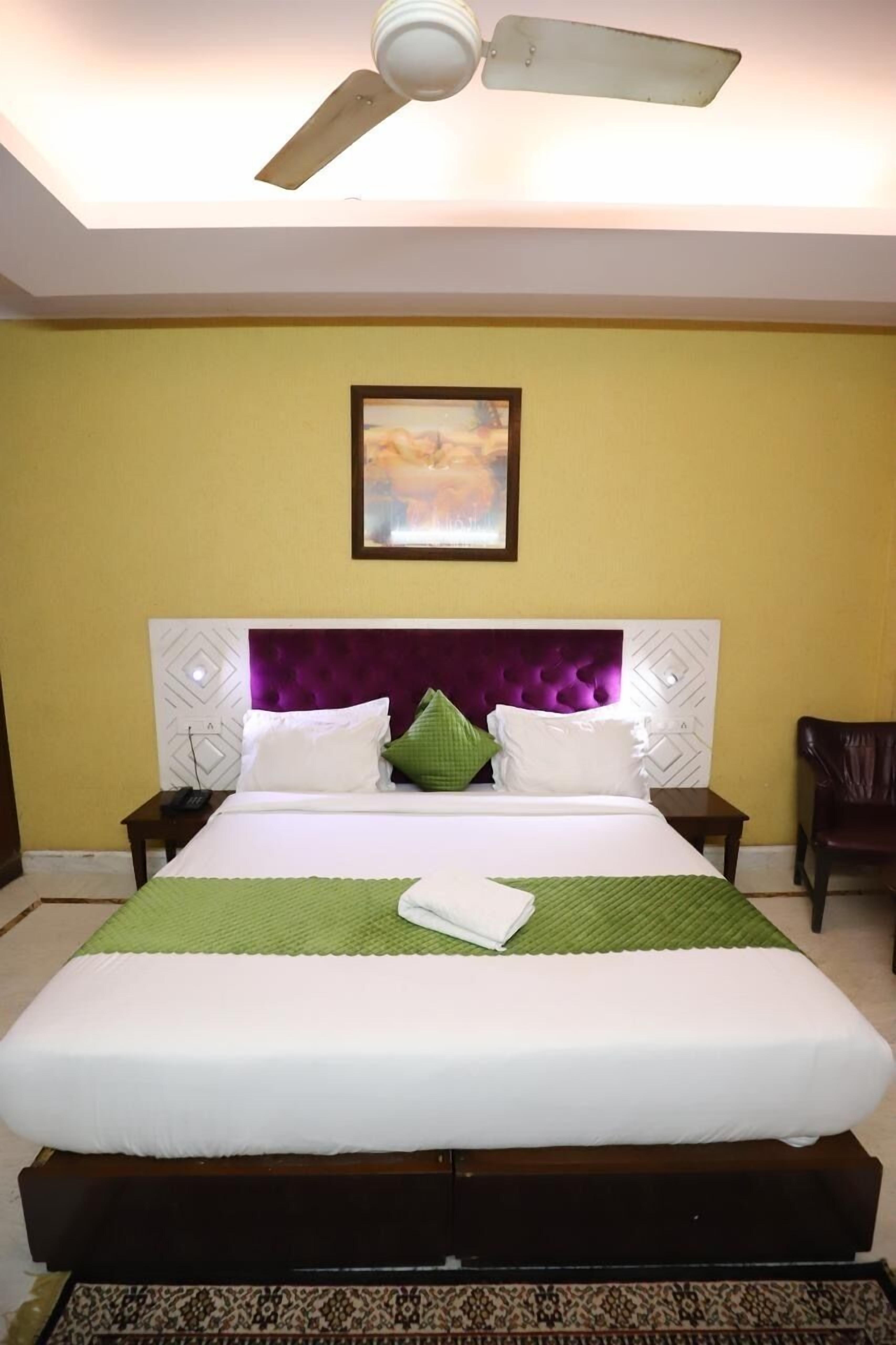 A neatly made bed with white and green bedding, a purple headboard, and a ceiling fan above.