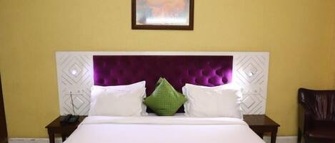 A neatly made bed with white and green bedding, a purple headboard, and a ceiling fan above.