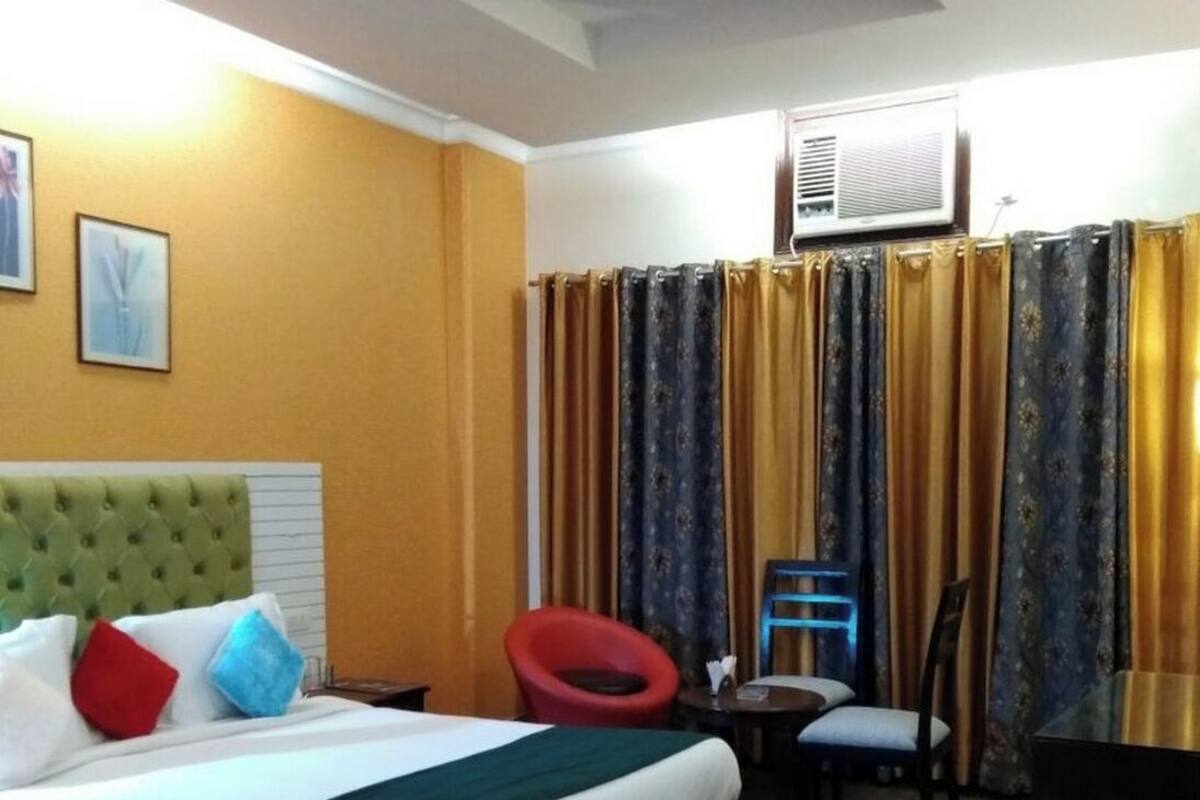 A hotel room with a bed, a red chair, a small table, and a ceiling fan.