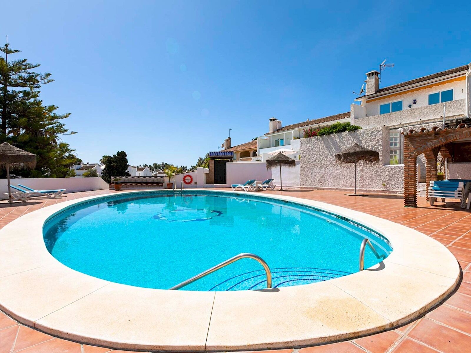 A swimming pool with a tiled deck, lounge chairs, and a small building with a chimney.