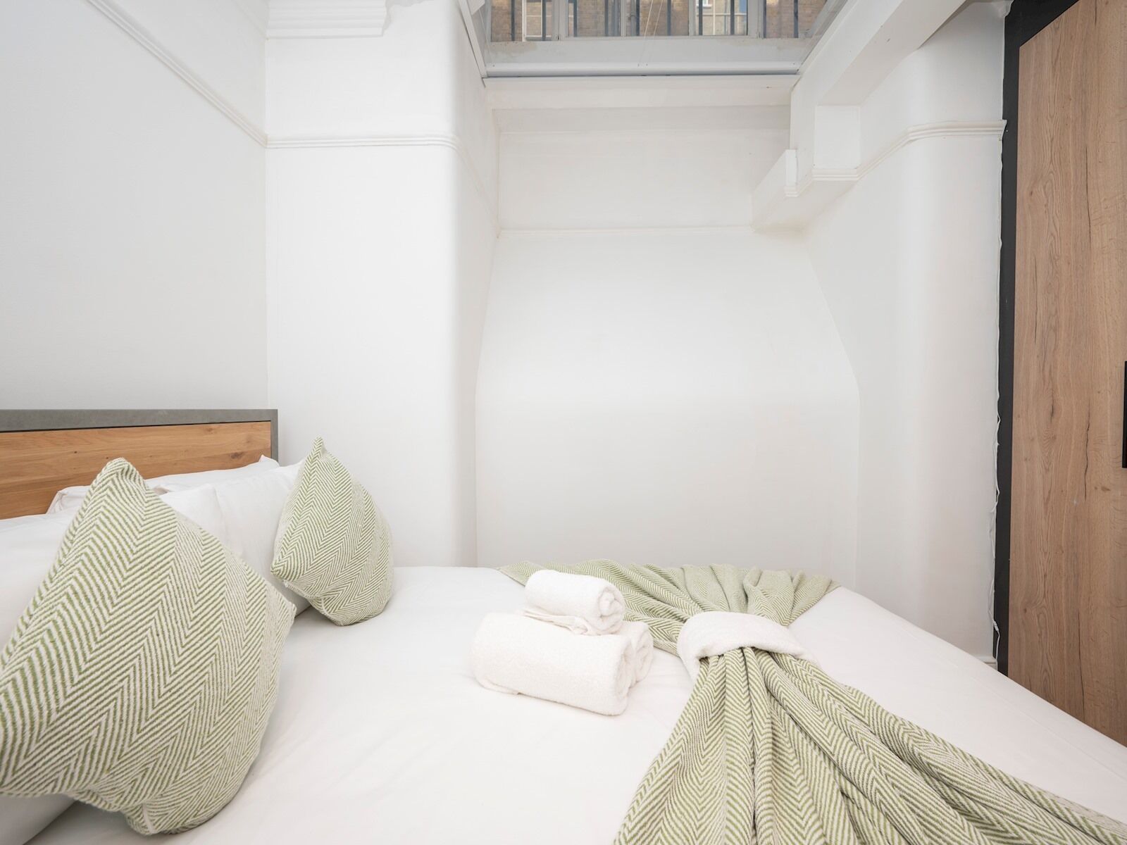 A hotel room with a bed, pillows, and a neatly made bed with towels.