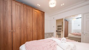 Ein Schlafzimmer mit großem Holzschrank, einem Bett mit rosa Bettwäsche und einem Spiegel, der den Raum wiedergibt.
