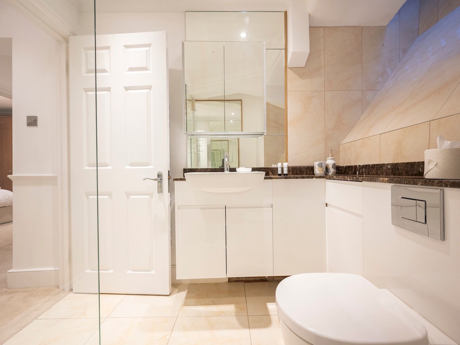 A modern bathroom with a white toilet, a sink, and a mirror above it. There is a door leading to another room.