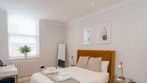 A modern bedroom with a large bed, bedside tables, a desk, and a window with blinds. - The Salisbury Sleeps 4 Classic Apartment (Scarborough)