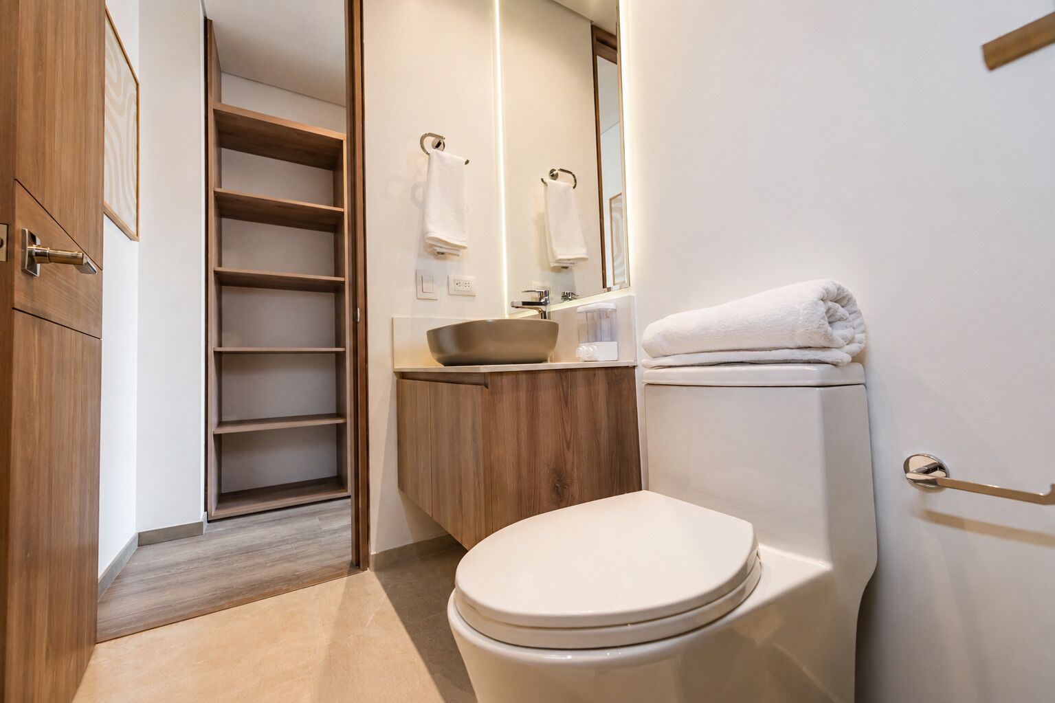 A modern bathroom with a toilet, sink, and built-in shelving.